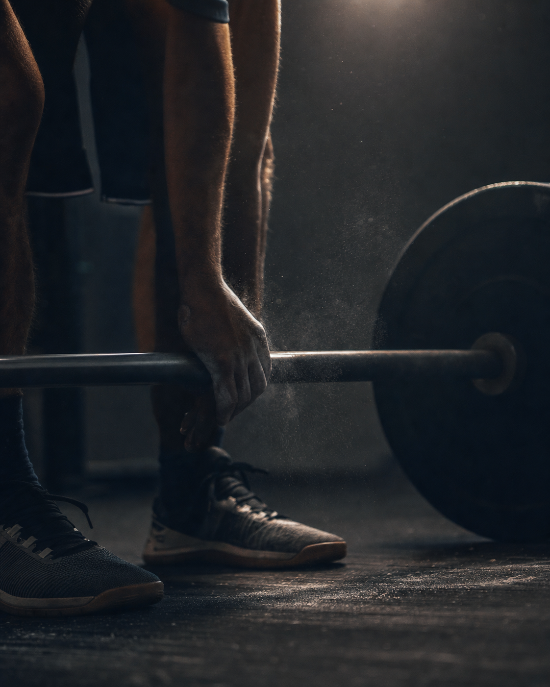 An athlete grips a barbell, chalk dust in the air.